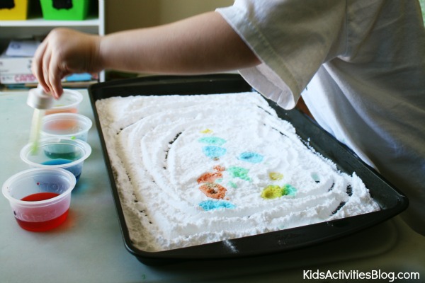 activités sensorielles avec du bicarbonate de soude et du vinaigre Étape 3 - Faites de l'art avec du bicarbonate de soude et du vinaigre - un enfant utilise un compte-gouttes pour déposer des gouttes de vinaigre sur du bicarbonate de soude de couleur vive avec du colorant alimentaire - Blog d'activités pour enfants