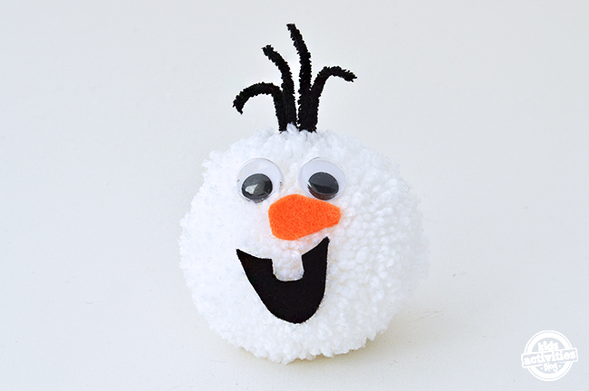 Olaf Frozen Pom Pom avec des yeux google, un nez en feutre orange carron, une bouche noire et des cheveux en feutre