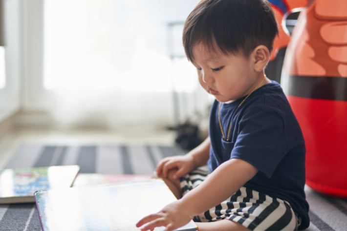 Lire un livre à bébé - blog d'activités pour enfants - bébé assis en train de lire un livre cartonné dans la salle de jeux