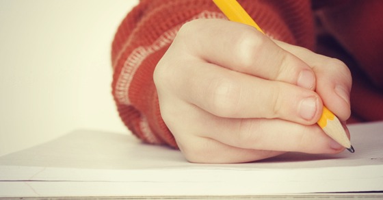 Mauvaise façon de tenir un crayon - position incorrecte courante que les enfants utilisent souvent - quatre doigts serrent le crayon au lieu de trois - montré en train d'écrire de manière incorrecte sur du papier de cahier