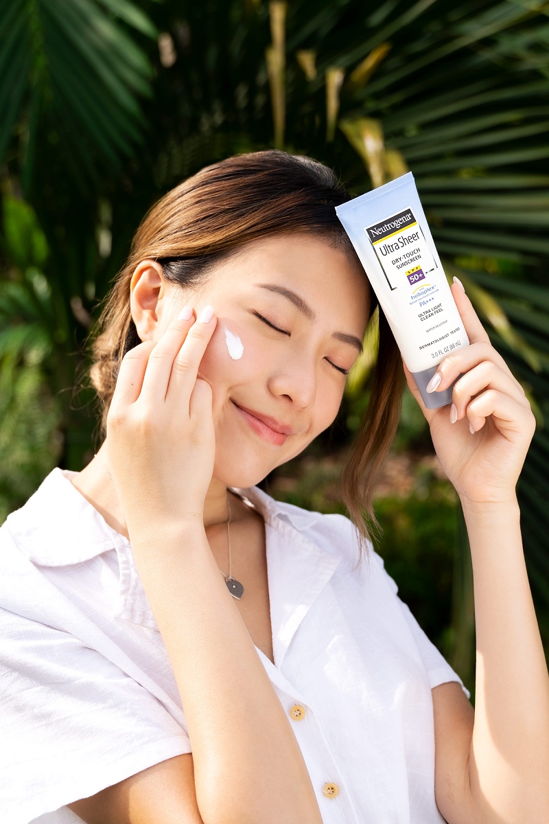 Une fille pose avec un écran solaire Neutrogena Ultra Sheer Dry Touch Neutrogena Singapore Holiday 2022 Crème solaire au toucher sec