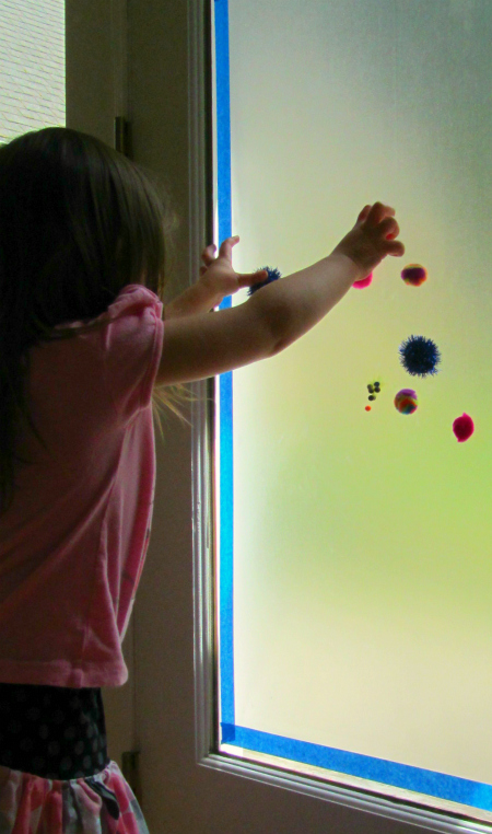 mur collant sur une fenêtre avec un enfant ajoutant des pompons moelleux de No Time for Flashcards