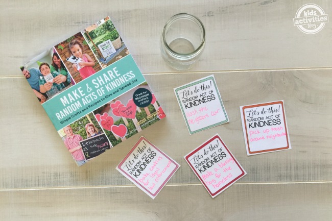 Texte : Family Kindness Jar- Book à côté d'un pot avec 4 morceaux de papier texte : Let's do this ! Acte de gentillesse aléatoire sur fond de bois - blog activités enfants