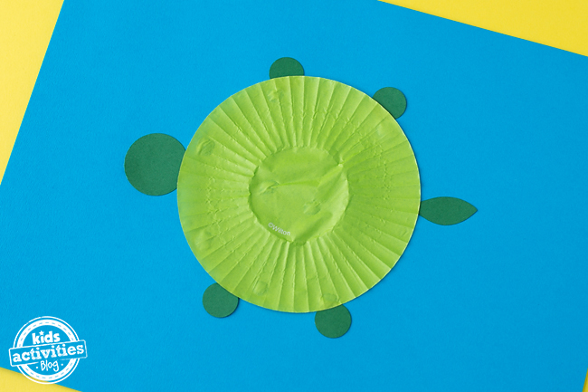 Cupcake Liner Turtle Craft - étape - ajoutez les jambes, la tête et la queue à votre doublure de cupcake aplatie et collez-les sur le blog d'activités pour enfants en papier bleu