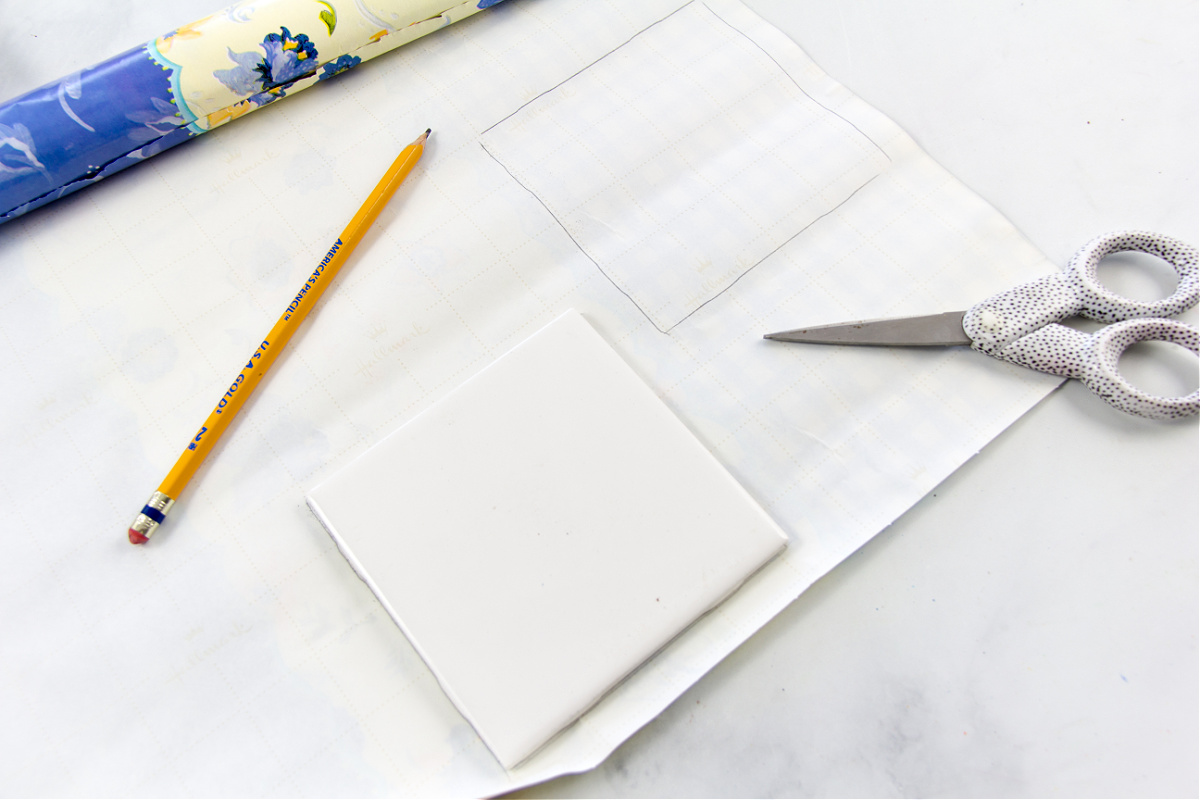 l'étape 1 pour fabriquer des sous-verres en carreaux consiste à tracer le contour des sous-verres sur l'emballage cadeau avec un crayon.