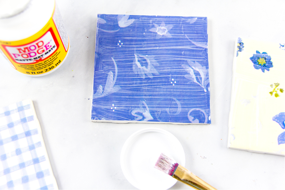 l'étape 4 pour fabriquer des dessous de verre consiste à ajouter des couches de mod podge sur le papier