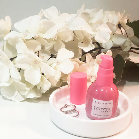 The Glow Recipe Guava Vitamin C Bright-Eye Gel Cream avec des fleurs et des anneaux d'argent dans un sous-verre