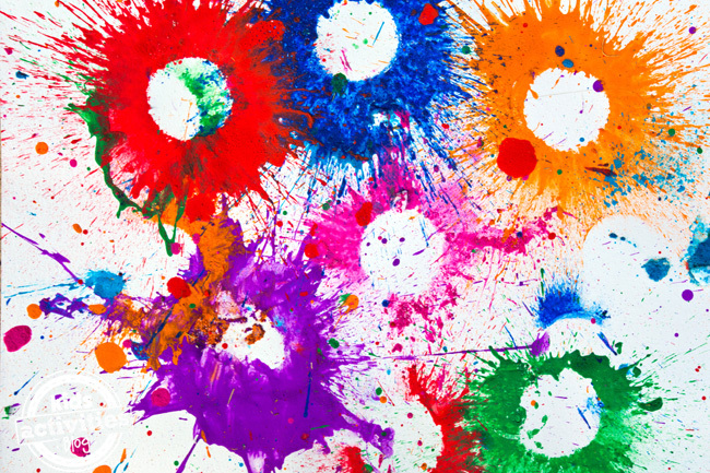 Texte : Bombes de peinture explosives - Blog d'activités pour enfants - Toile avec des éclaboussures d'orange, de bleu, de vert, de rose, de rouge et de violet
