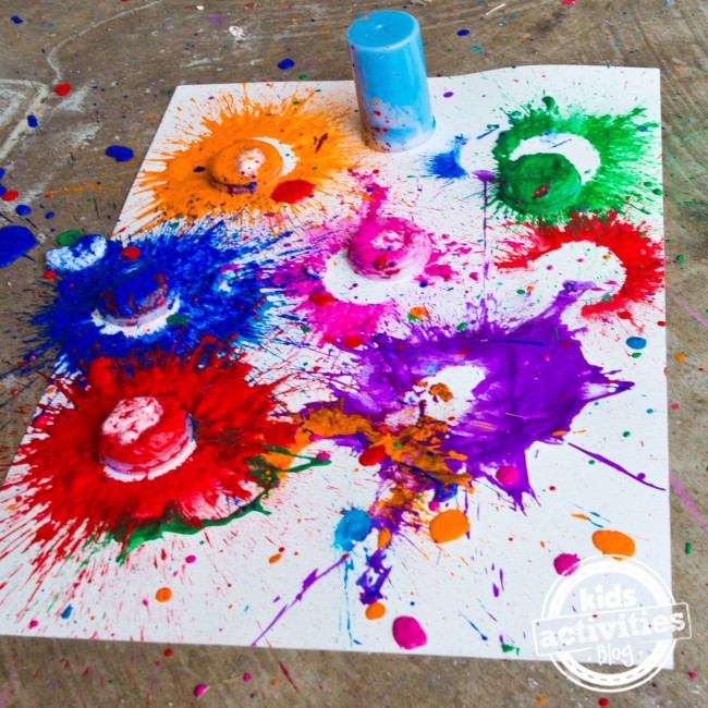 Texte : Bombes de peinture explosives - Blog d'activités pour enfants - Toile avec des éclaboussures d'orange, de bleu, de vert, de rose, de rouge et de violet - avec des gobelets et des couvercles en plastique