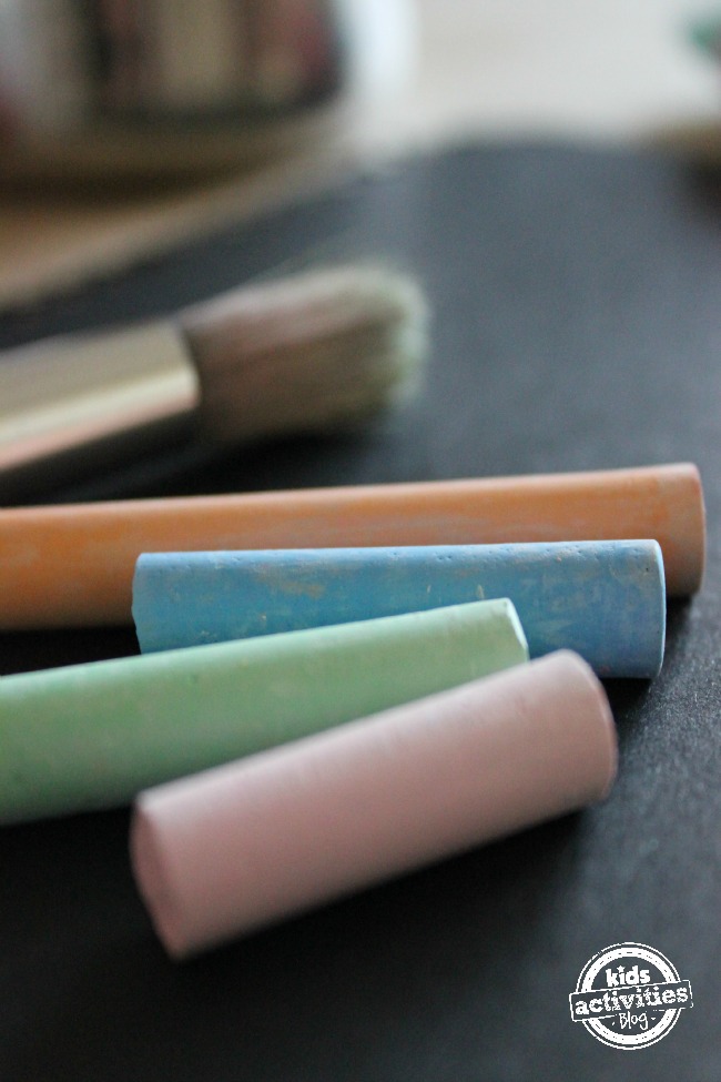 utiliser de la craie dans l'art- Fournitures de peinture à la craie- Papier noir- craie orange, bleue, verte et rose, avec des pinceaux- blog d'activités pour enfants