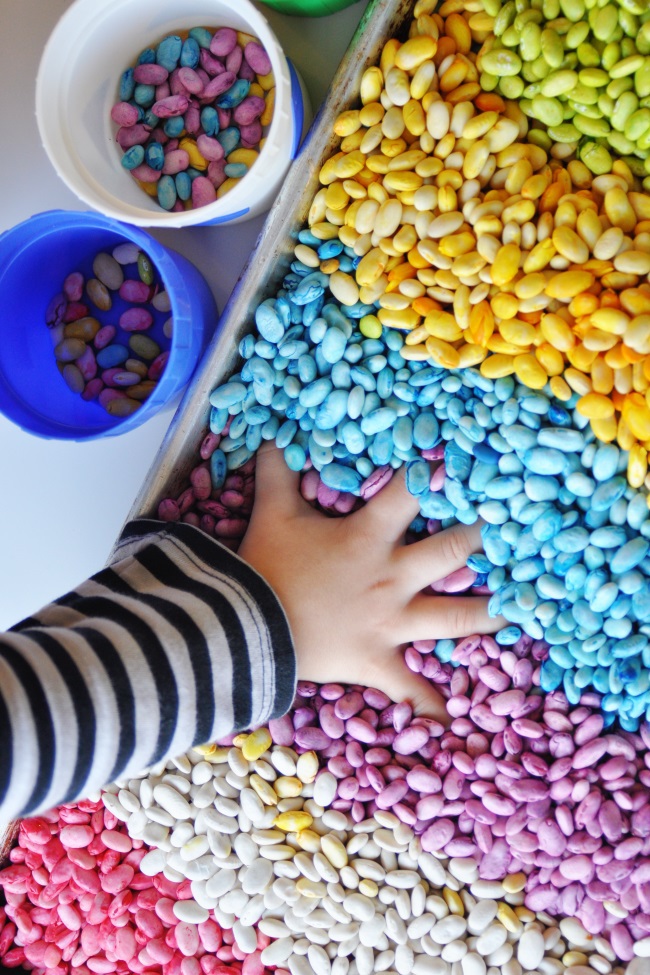 Haricots arc-en-ciel parfumés sensoriels aux couleurs de l'arc-en-ciel - main d'enfant jouant dans un tas de haricots colorés - Blog d'activités pour enfants