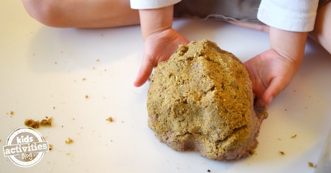 Recette de sable cinétique maison qui utilise du sable de jeu et de la boue mélangés par les mains d'un enfant.
