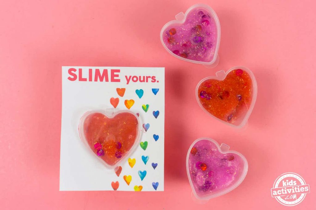 Ces valentines en slime sont super mignonnes. C'est du slime rouge et rose avec des étincelles dans des récipients en forme de cœur sur une carte Slime yours Valentines.