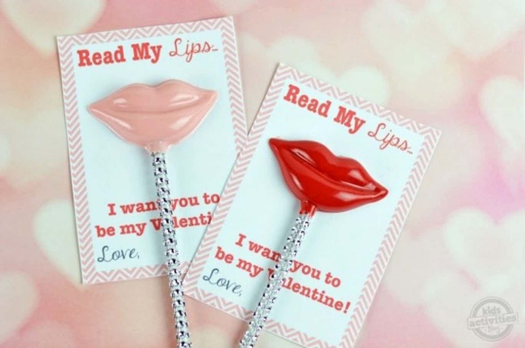 Valentines à lèvres imprimables qui disent lire mes lèvres, je veux que tu sois ma Saint-Valentin. Il y a un bonbon à lèvres au chocolat rouge et rose dessus avec un bâtonnet de gâteau à paillettes qui le tient.