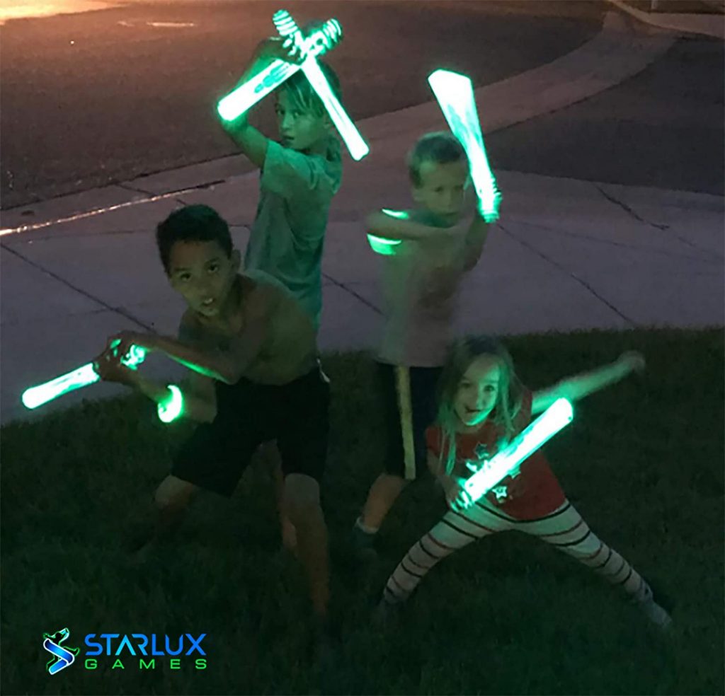 3 garçons et 1 fille étant des samouraïs ninja avec leurs bâtons lumineux jouant à des jeux de ninja pour les enfants sur la pelouse