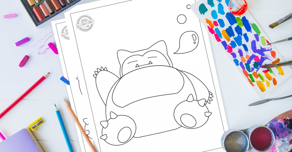 Pack de pages à colorier Snorlax Pokemon sur un bureau entouré d'outils de coloriage comme des pastels, des crayons de couleur, de la peinture et des outils d'art. La page de coloriage supérieure présente le pokémon géant à câliner Snorlax