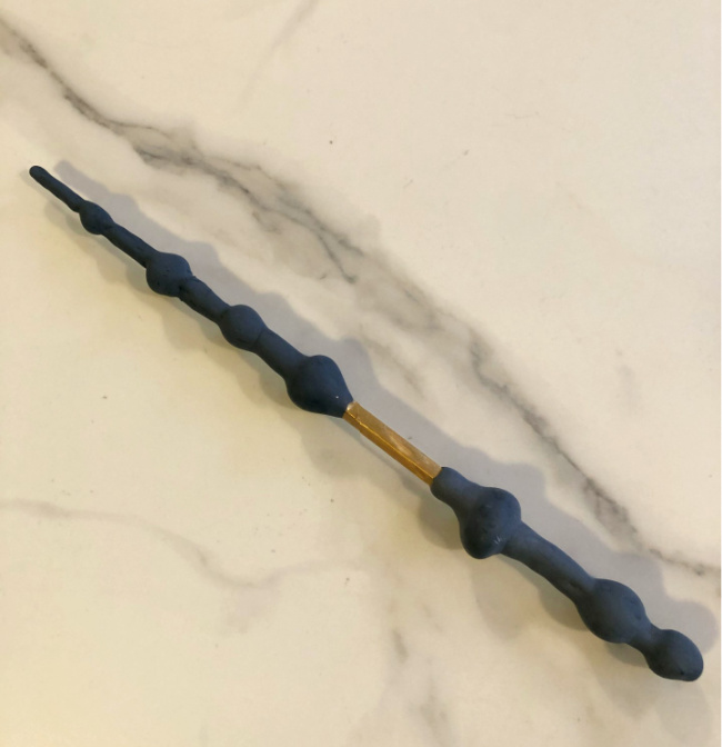 Baguette de Harry Potter Elder sur un comptoir en marbre blanc.  Baguette grise avec des bosses et une marque d'or vers la moitié inférieure.