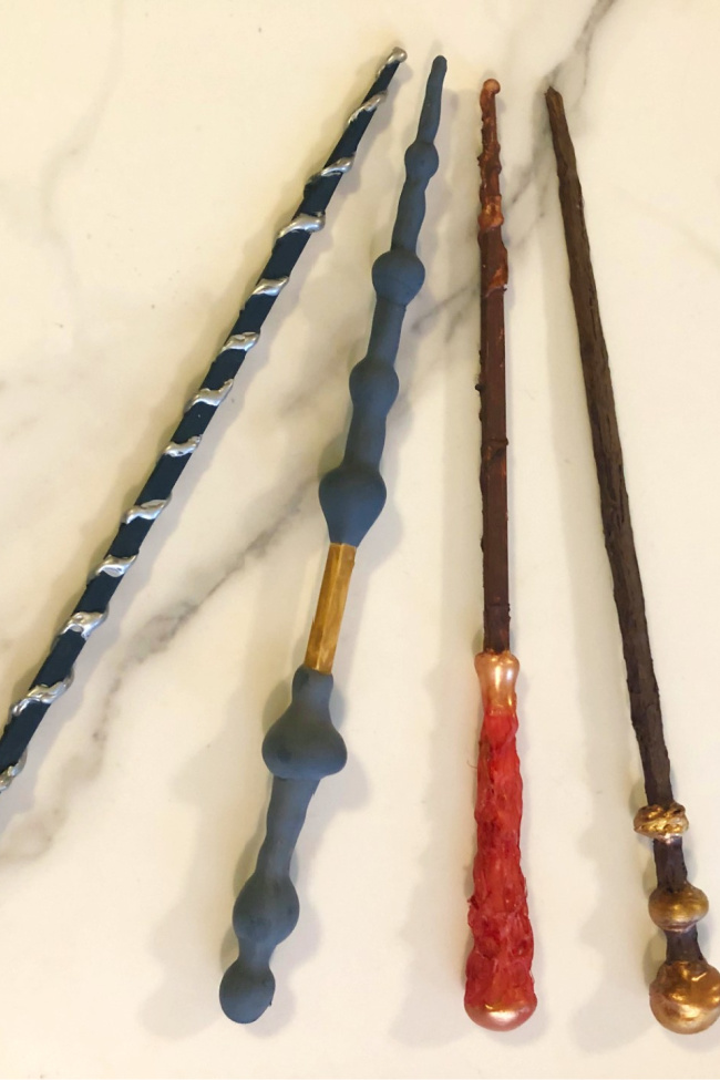 Baguettes Harry Potter sur un comptoir en marbre.  De gauche à droite, une baguette noire avec des tourbillons argentés, la baguette de sureau grise avec une bande dorée, une baguette marron avec une poignée rouge et une baguette marron avec des boules dorées à la fin.