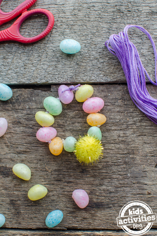 Bracelet de Pâques en fèves à la gelée vertes, roses, jaunes et orange présentées sur une table en bois - Kids Activities Blog