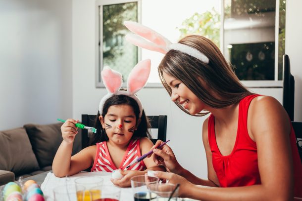 Une mère et sa fille avec des oreilles de lapin peignant des décorations d'œufs de Pâques sur des œufs durs.