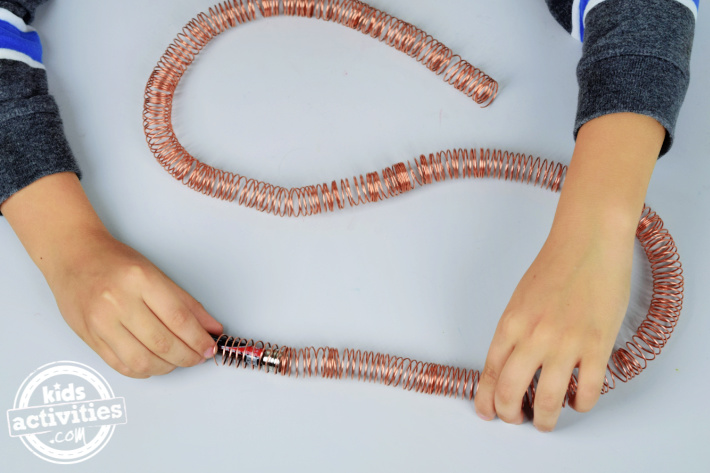 Étape 3 - Créer une voie de train en bobine de cuivre - Instructions de train électromagnétique - Blog d'activités pour enfants - grande bobine de fil de cuivre enroulée autour du dessus de la table avec un enfant démarrant le train de batterie