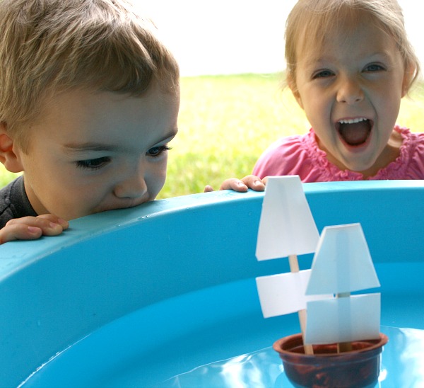 Artisanat de bateau Mayflower pour les enfants de Fantastic Fun and Learning - deux enfants regardent le bateau qu'ils ont construit qui ressemble au flotteur Mayflower dans une piscine pour enfants dans la cour avant