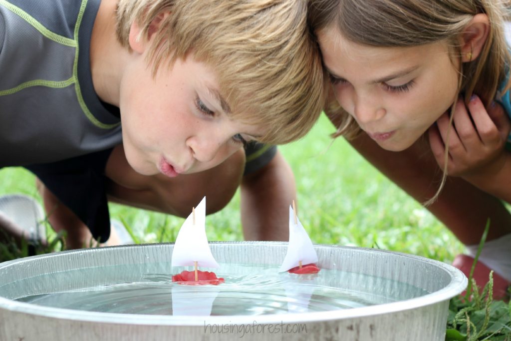 Wax-Boats-for-Kids-from Housing a Forest - deux enfants soufflant sur des bateaux de cire flottant dans une baignoire en métal dans la cour
