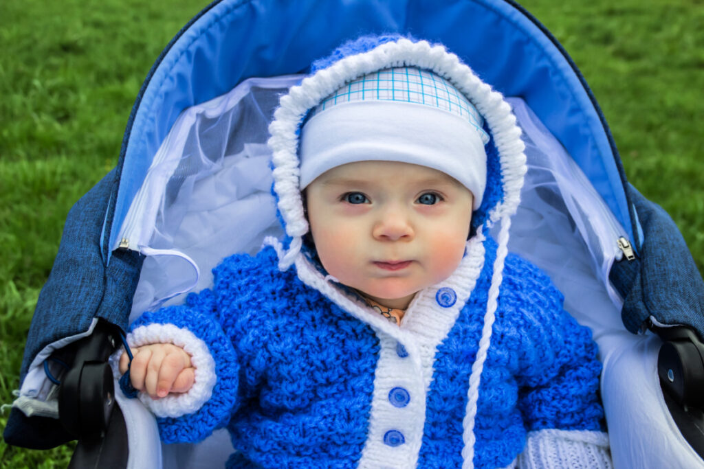 Bébé dans une poussette - Blog d'activités pour enfants - bébé en tenue bleue dans une poussette sur l'herbe verte en regardant la caméra