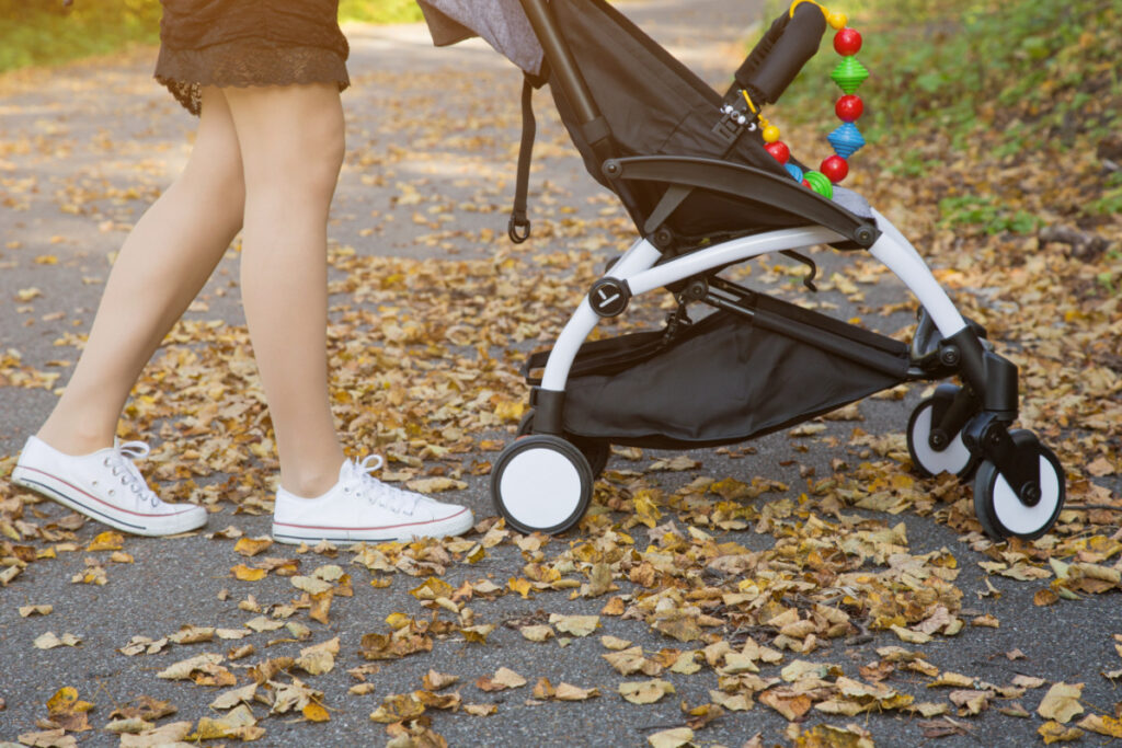 Maman poussant la poussette - Blog d'activités pour enfants - bas de la poussette et jambes de la mère poussant la poussette sur le trottoir avec des feuilles