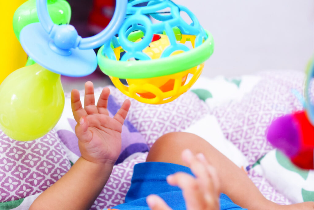 Panier de jouets et balle - Blog d'activités pour enfants - mains et jambes de bébé cherchant des jouets suspendus