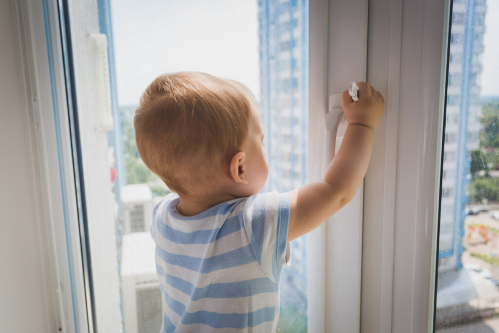 Bébé regardant par la fenêtre - Blog d'activités pour enfants - bébé avec les mains sur le cadre de la fenêtre regardant dehors