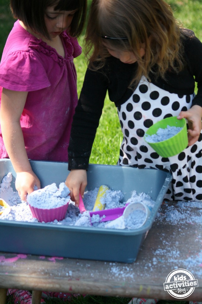 Toddler-Safe Cloud Dough s'est transformé en un bac sensoriel avec des moules à cupcakes en silicone, des tasses, des pelles et des bâtons.
