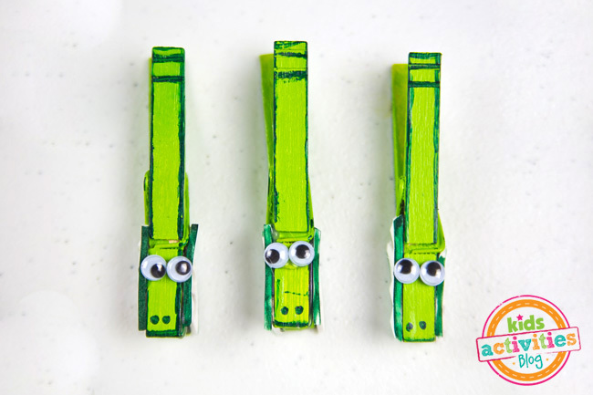 Étape 5 - Artisanat d'alligator peint en vert, délimité par un marqueur vert, des yeux écarquillés et des dents en mousse blanche.