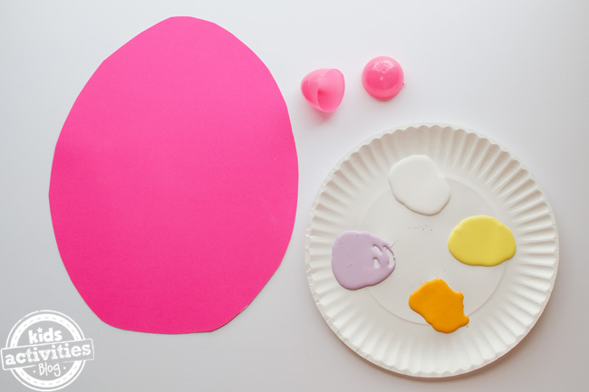 étape 2 - artisanat d'oeufs de pâques préscolaire - découpez la forme d'oeuf de pâques sur du papier de construction rose montré à côté de la plaque de papier de peinture avec des couleurs - blanc, lavande, orange et jaune