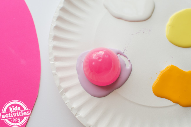 étape 3 - artisanat d'œufs de pâques préscolaire - œuf en plastique à moitié trempé dans une tache de peinture sur une assiette en papier