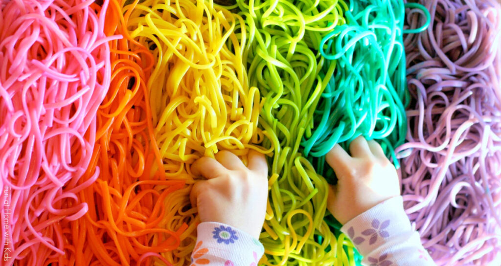 Activité sensorielle de pâtes colorées - Fun at Home with Kids - mains d'enfant en spaghetti aux couleurs rose, orange, jaune, vert, bleu et violet