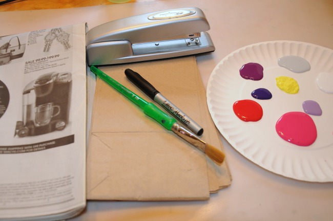 Fournitures pour créer une ville imaginaire avec des sacs en papier - sacs en papier, pinceaux, marqueurs, peinture sur une assiette en papier (rose, rouge, noir, blanc, violet, marron, gris), un marqueur noir, un journal et une agrafeuse