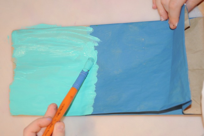 Étape 1 - Paper Bag House Craft - Peindre des sacs en papier pour ressembler à des bâtiments dans votre ville - le sac est peint en aigue-marine et bleu ciel avec un pinceau orange.