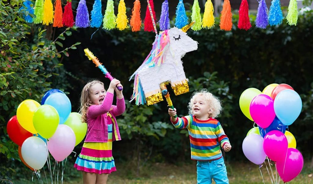 Pinata licorne présentée lors d'une fête d'anniversaire licorne avec des banderoles et des ballons et des enfants frappant la pinata avec des bâtons colorés