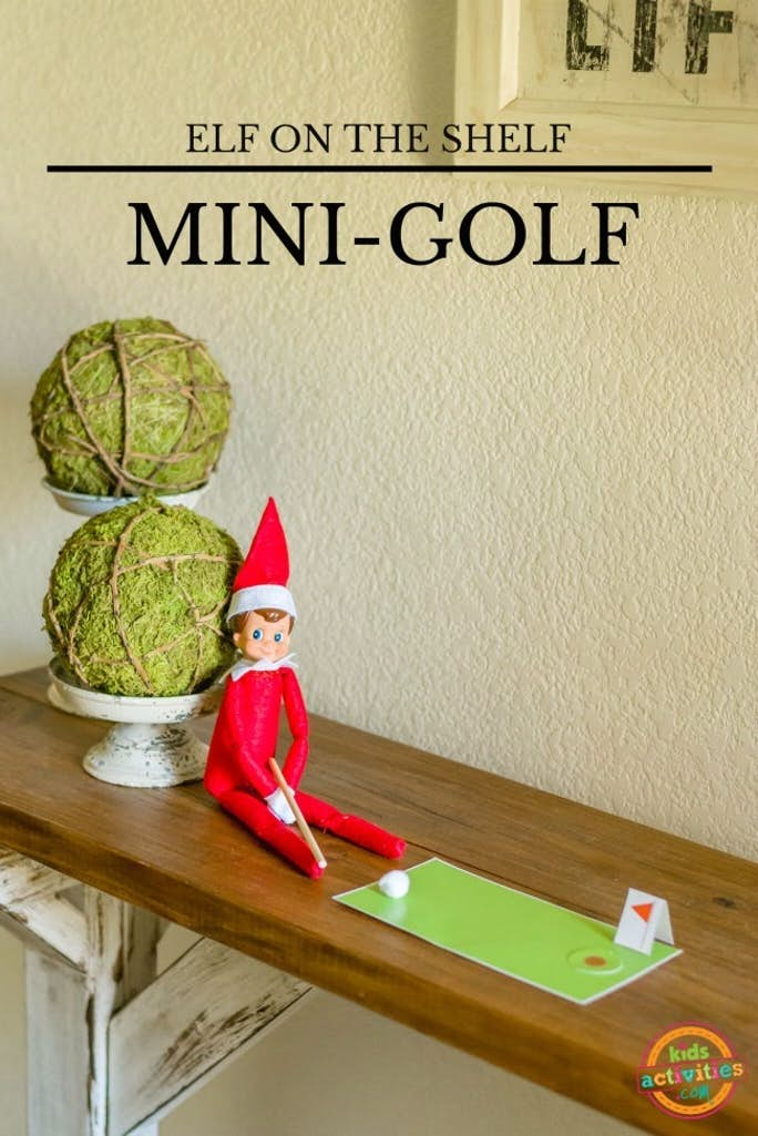Parcours de golf d'Elfe sur l'étagère et golf imprimable installés sur une étagère en bois avec de l'herbe verte imprimable, un trou imprimable et un drapeau imprimable avec un putter de cure-dents en bois et un petit pompon comme balle de golf : texte : Mini-golf d'Elfe sur l'étagère - blog d'activités pour enfants