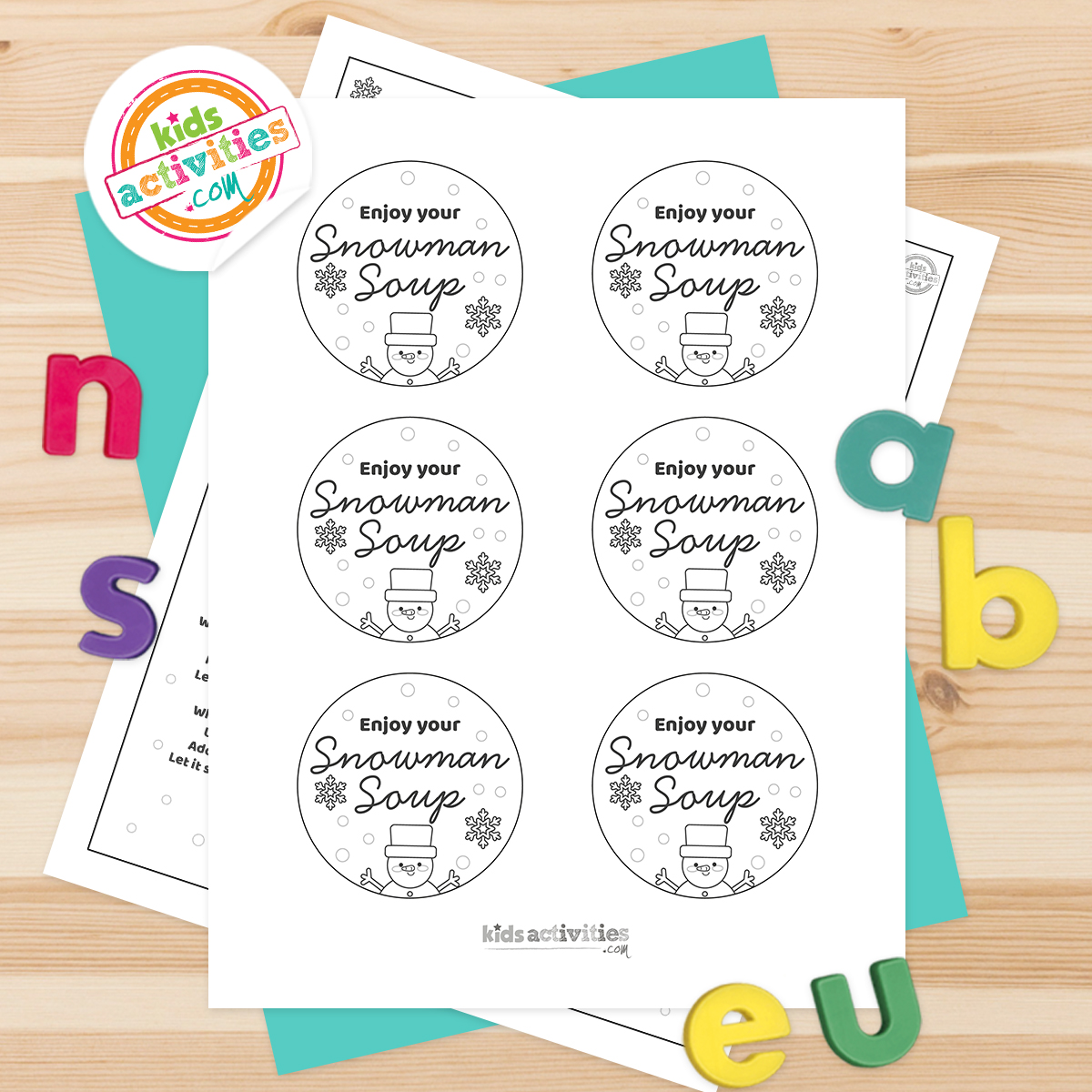Autocollants de soupe bonhomme de neige noir et blanc imprimables, posés sur une feuille bleu-vert avec des lettres multicolores sur fond marron clair.  version pdf imprimée du blog d'activités pour enfants. 

