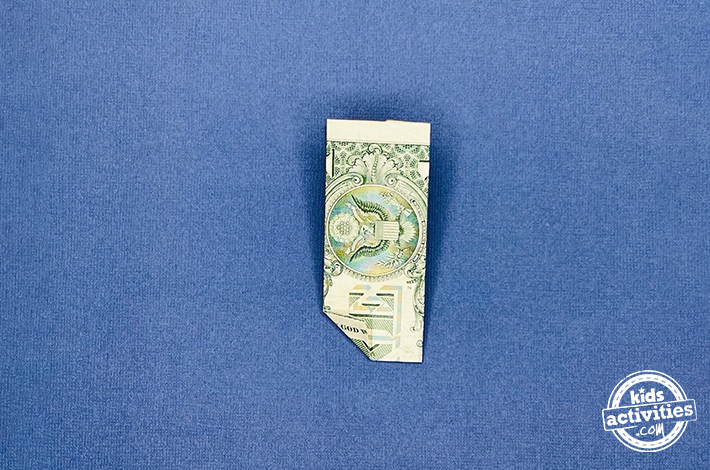 Pantalon origami en forme de billet d'un dollar - Étape 5 - Pliez le coin inférieur gauche vers le haut, puis dépliez-le pour créer un pli.