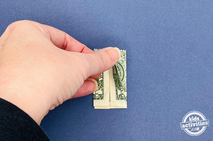 Pantalon origami en forme de billet d'un dollar - Étape 7 - Pliez la couche supérieure en deux, en vous assurant que les deux côtés sont symétriques. Retournez la figurine et répétez ce pli de l'autre côté.