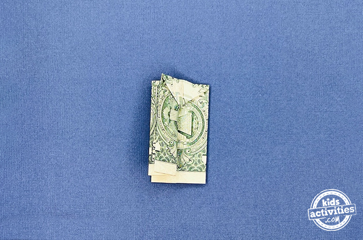 Pantalon origami en forme de billet d'un dollar - Étape 7 - Pliez la couche supérieure en deux, en vous assurant que les deux côtés sont symétriques. Retournez la figurine et répétez ce pli de l'autre côté.