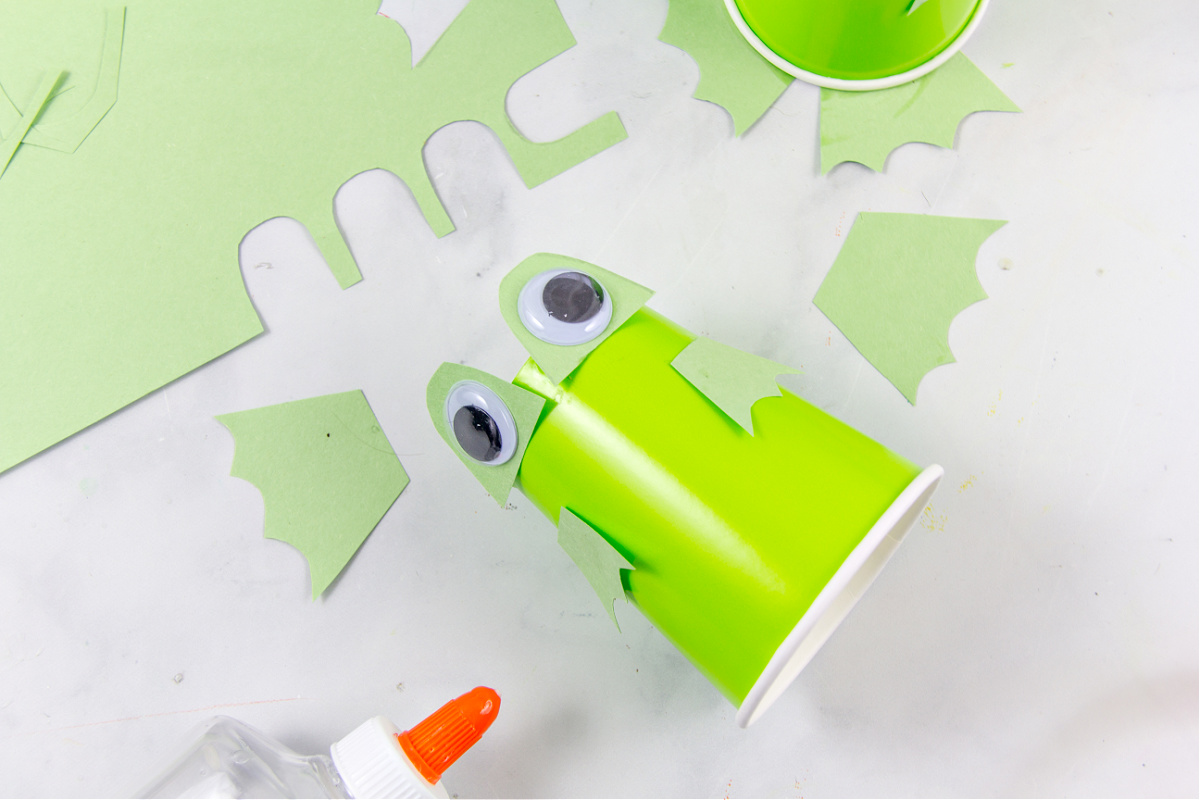 L'étape 2 pour fabriquer un gobelet en papier en forme de grenouille consiste à coller les parties de la grenouille sur le gobelet en papier vert.