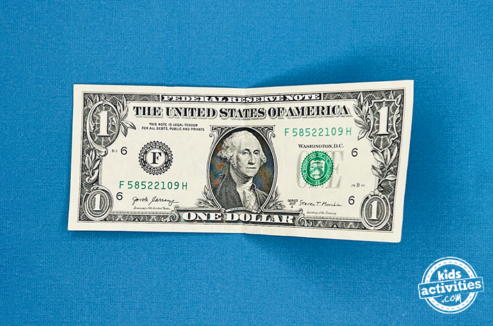 Cygne en origami billet d'un dollar - Étape 1 - Dépliez-le pour faire un pli. Tutoriel du blog d'activités pour enfants.