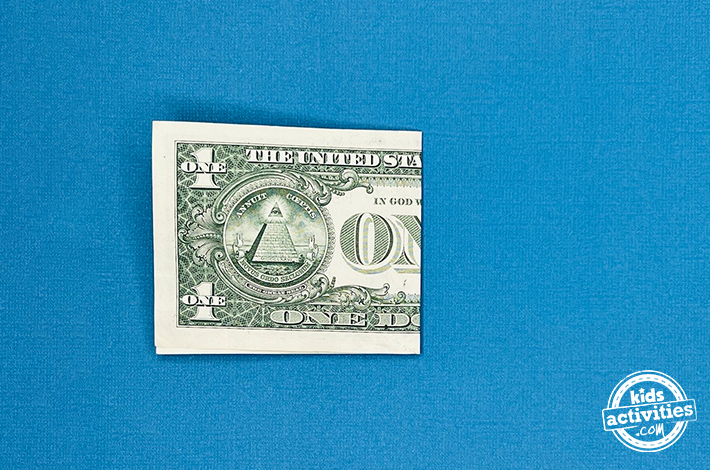 Cygne en origami pour billet d'un dollar - Étape 1 - Pliez le billet en deux pour faire un pli. Tutoriel du blog d'activités pour enfants.