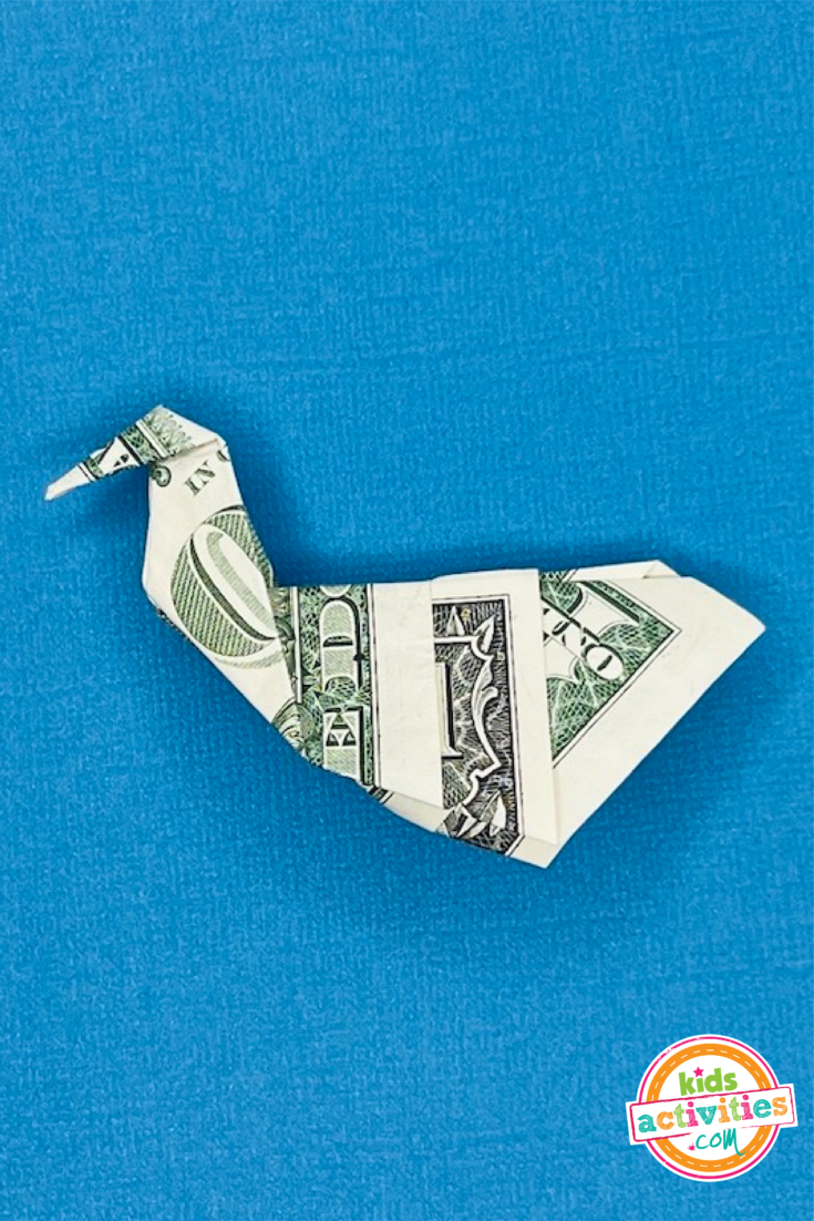 Résultat final pour un cygne en origami en forme de billet d'un dollar sur un fond bleu.  Tutoriel du blog d'activités pour enfants