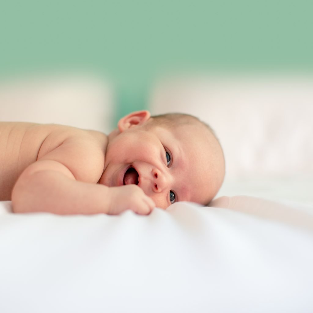 bébé rit en étant allongé sur un lit blanc avec fond vert