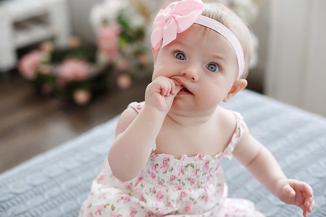 bébé assis avec la main dans la bouche